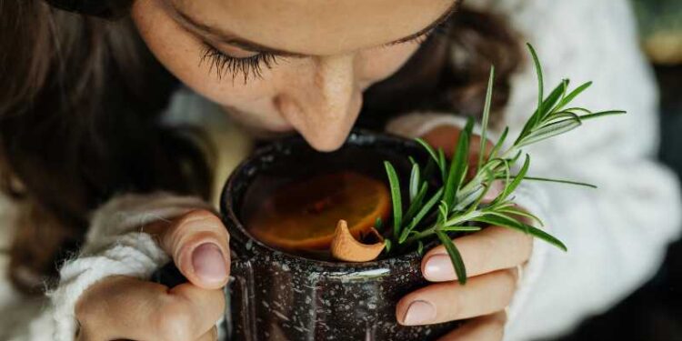 Woman savoring hot herbal tea with rosemary and orange, close-up view., tags: für - pexel